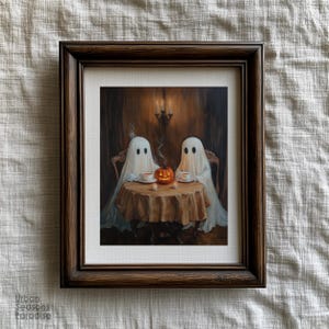 May include: A framed print depicts two ghosts seated at a table, enjoying tea with a carved pumpkin centerpiece. The artwork is set in a dimly lit room with a chandelier and a dark brown wooden frame. The print is a Halloween-themed artwork.