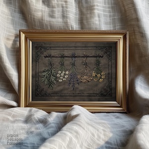 May include: A rectangular gold-toned frame containing an embroidery piece on a dark gray fabric. The embroidery depicts five bundles of dried herbs and flowers hanging from a horizontal rod, enclosed within a decorative black stitched border.