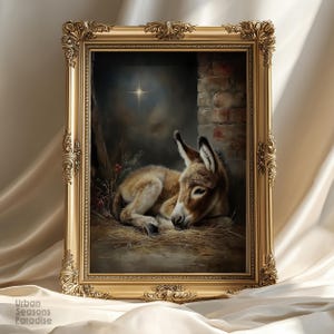 Puede incluir: Obra de arte enmarcada en un marco dorado ornamentado, que representa un burro descansando en un establo. El burro es de color marrón claro con orejas oscuras, acostado sobre paja. Una estrella brilla en el fondo.
