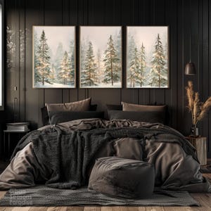Puede incluir: Tres impresiones art&iacute;sticas enmarcadas que representan una escena de bosque invernal con &aacute;rboles cubiertos de nieve y una iluminaci&oacute;n suave. La obra de arte cuelga sobre una cama con ropa de cama gris oscuro, una manta de punto y un otom&aacute;n redondo. La habitaci&oacute;n tiene paneles de madera oscura.