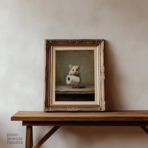 Op de afbeelding: Een ingelijste kunstdruk met een kleine, lichtgekleurde muis die op een houten oppervlak staat en een rol wit toiletpapier vasthoudt. Het kunstwerk zit in een sierlijke, goudkleurige lijst met gedetailleerde, uitgesneden versieringen.