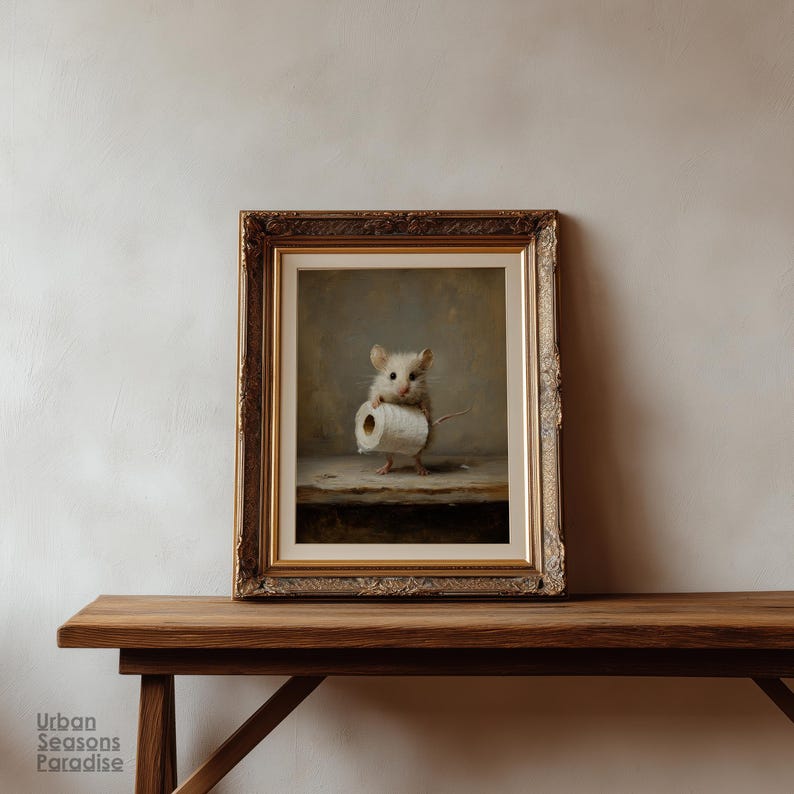 Op de afbeelding: Een ingelijste kunstdruk met een kleine, lichtgekleurde muis die op een houten oppervlak staat en een rol wit toiletpapier vasthoudt. Het kunstwerk zit in een sierlijke, goudkleurige lijst met gedetailleerde, uitgesneden versieringen.