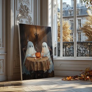 May include: A canvas print depicts two ghost figures seated at a table with a pumpkin and teacups. The artwork has a warm, inviting color palette with a vintage aesthetic. The print is leaning against a wall near a window with a view of a European building.