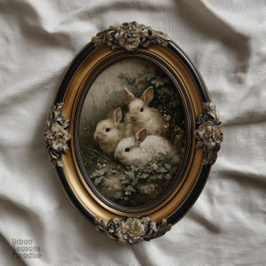 May include: Oval framed artwork featuring three white rabbits nestled in greenery. The frame has a black and gold finish with floral embellishments. The artwork has a vintage, antique aesthetic.