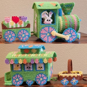 Puede incluir: Un tren de Pascua verde y amarillo con decoraciones de conejito y pollito. El tren tiene tres vagones, incluyendo un furgón de cola con un asa de cesta. El tren está hecho de lona de plástico y está decorado con flores y huevos.