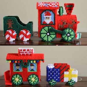 Könnte beinhalten: Ein Set handgefertigter Weihnachtszug-Ornamente. Die Lokomotive ist rot mit einem Weihnachtsmann-Design, grünen Rädern und einem grünen Schornstein. Die Waggons sind rot, grün und blau mit festlichen Details. Die Ornamente sind aus Kunststoff-Leinwand.