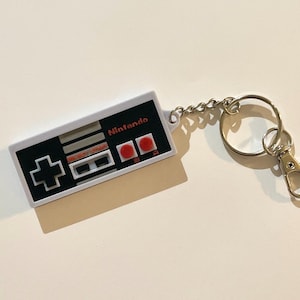 ユニークなレトロ任天堂コントローラーキーチェーン - 懐かしいクラシックNESゲームの雰囲気を細部まで再現し、高解像度で3Dプリントされています。