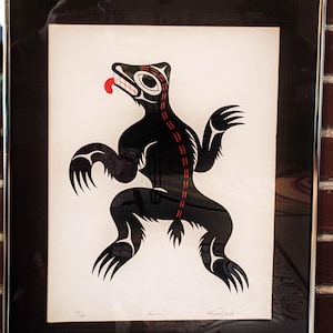 Puede incluir: Ilustración estilizada en negro y rojo de un oso con una lengua roja, enmarcada en un marco negro con un borde plateado. La obra de arte está firmada "Bear" y "Beadle" en la esquina inferior derecha.