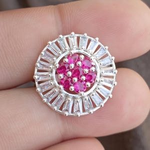 Puede incluir: Un anillo de plata con un diseño redondo que presenta un grupo de piedras preciosas rosas rodeadas de piedras transparentes en forma de baguette.