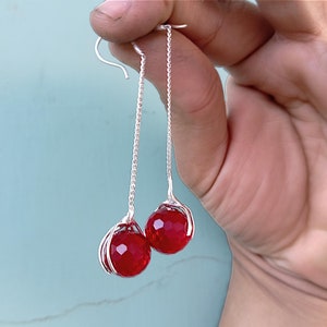 Puede incluir: Un par de pendientes de plata con gotas de piedras preciosas rojas. Los pendientes presentan un diseño delicado de alambre.