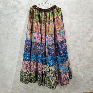 May include: A floor-length tiered skirt featuring a patchwork design with various colorful patterns including paisley, floral, and geometric prints in shades of green, pink, blue, purple, and gold, finished with an elasticized waistband.