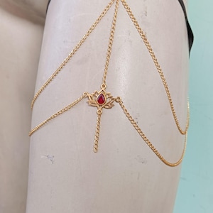 May include: Gold chain body jewellery with a red gem lotus pendant.