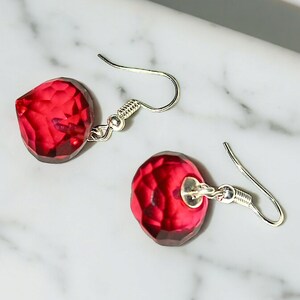 May include: A pair of silver earrings with red faceted crystal drops. The earrings have a simple hook fastening.
