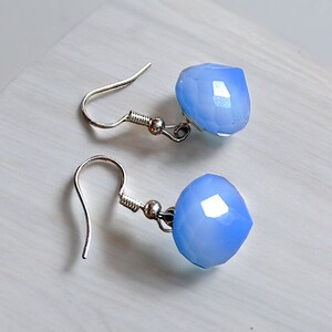 Puede incluir: Un par de pendientes de plata con gotas de piedras preciosas facetadas de color azul claro.