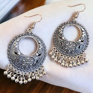 Può includere: Un paio di orecchini d'argento con un design circolare e una catena di perline pendenti. Gli orecchini hanno un motivo floreale e un grande cerchio aperto al centro.