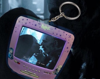 May include: A purple Bratz-branded keychain with a miniature, retro television design. The screen shows a black and white image of a kissing couple, with the text "Your blood tempts my name." The keychain includes a silver ring.