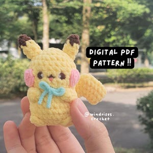 Może przedstawiać: Ręcznie robiony żółty szydełkowy pluszowy Pikachu z brązowymi uszami, różowymi policzkami i niebieską kokardą. Tekst "DIGITAL PDF PATTERN !!" jest wyświetlany na czarnym prostokącie. Pluszak jest trzymany w dłoni.