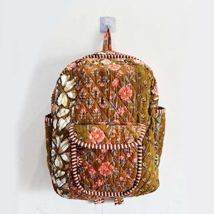 以下が含まれることがあります： 茶色、ピンク、白の色合いの花柄のキルティングバックパック。 バックパックにはフロントポケットとサイドポケットがあります。 ストラップとトリムはストライプのデザインです。