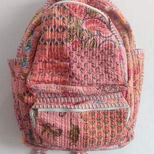Peut inclure: Un sac à dos matelassé rose avec un imprimé floral et tigre. Le sac à dos a deux poches zippées à l'avant et un grand compartiment principal.