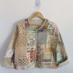 Könnte beinhalten: Eine beige gesteppte Jacke mit Patchwork-Design, das verschiedene florale Muster in Braun-, Rosa-, Blau- und Grüntönen zeigt. Die Jacke hat einen Knopfverschluss und zwei aufgesetzte Taschen.