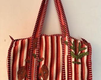 Könnte beinhalten: Gesteppte Tragetasche mit rot-weißen vertikalen Streifen. Die Tasche hat gestickte Blumen- und Blattmotive in Orange und Grün. Die Griffe sind ebenfalls rot und weiß gestreift.