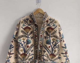 May include: A cream-colored jacket with intricate floral embroidery in shades of blue, green, brown, and red. The jacket has a mandarin collar and long sleeves.