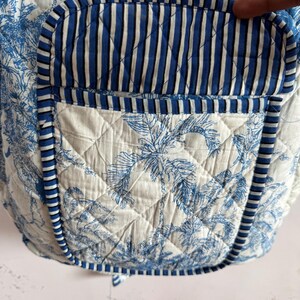 Peut inclure: Tissu matelass&eacute; avec un motif de palmiers tropicaux bleus et blancs. La poche pr&eacute;sente un motif &agrave; rayures bleues et blanches. Les bords sont bord&eacute;s d'une bordure ray&eacute;e bleue et blanche. Le tissu est matelass&eacute; avec un motif en losange.