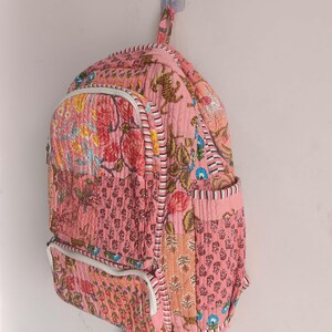 以下が含まれることがあります： ピンク色の花柄と虎柄のキルティングバックパック。 バックパックには、フロントジッパーポケット、白いトリム、調節可能なストラップが付いています。 バッグは壁に掛けられています。