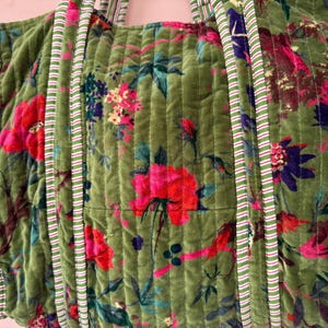 May include: Green quilted tote bag with a floral pattern featuring pink and red flowers, blue and purple accents, and green leaves. The bag has striped handles and trim.