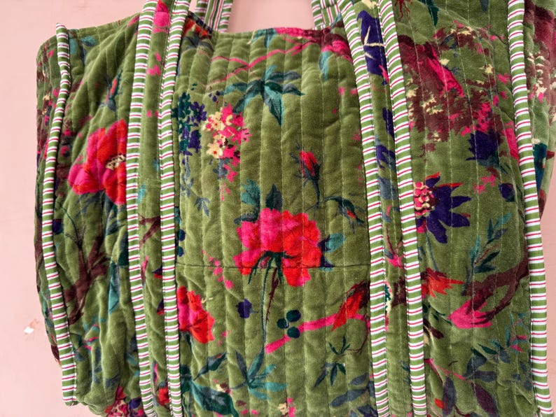 May include: Green quilted tote bag with a floral pattern featuring pink and red flowers, blue and purple accents, and green leaves. The bag has striped handles and trim.