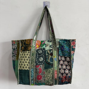 Könnte beinhalten: Eine Patchwork-Tragetasche mit verschiedenen floralen und geometrischen Mustern in Grün-, Blau-, Rot- und Brauntönen. Die Tasche hat zwei gestreifte Griffe und hängt an einer weißen Wand.