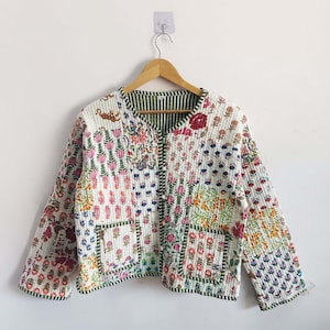 Peut inclure: Une veste matelassée blanche à imprimé floral. La veste est doublée de vert et se ferme par un bouton.