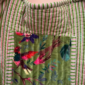 May include: Green and white striped tote bag with a floral pocket featuring a bird design. The bag has a quilted texture and red accents. The pocket showcases a colorful bird and foliage.
