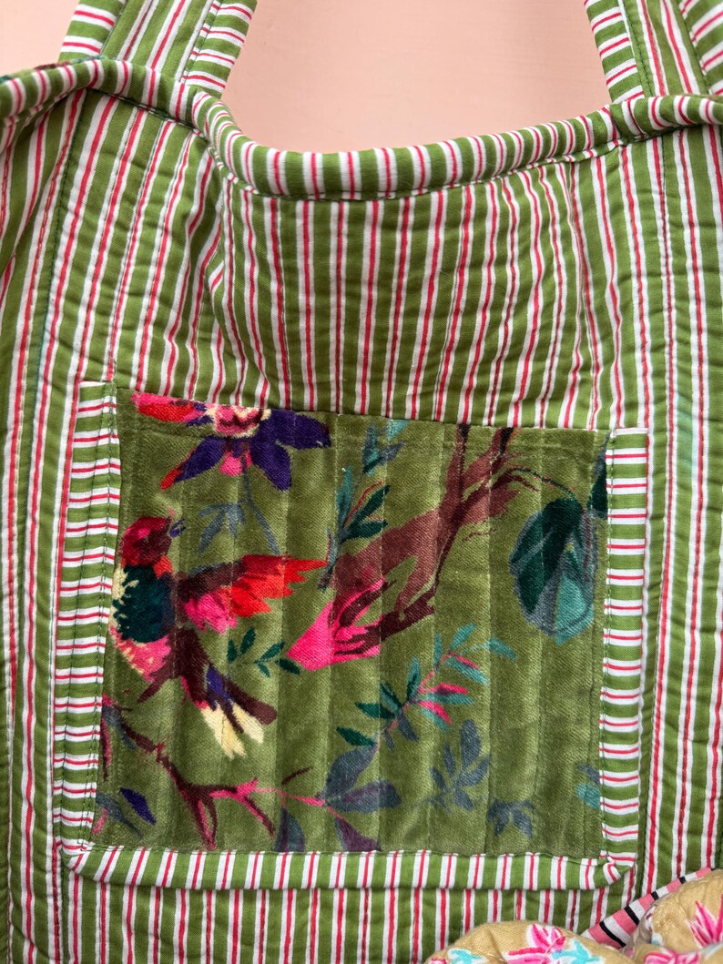 May include: Green and white striped tote bag with a floral pocket featuring a bird design. The bag has a quilted texture and red accents. The pocket showcases a colorful bird and foliage.