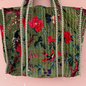May include: A large, quilted tote bag with a floral and bird pattern in shades of green, red, and blue. The bag has striped trim and handles. The bag is approximately 18 inches wide and 15 inches tall.