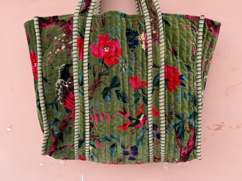 May include: A large, quilted tote bag with a floral and bird pattern in shades of green, red, and blue. The bag has striped trim and handles. The bag is approximately 18 inches wide and 15 inches tall.