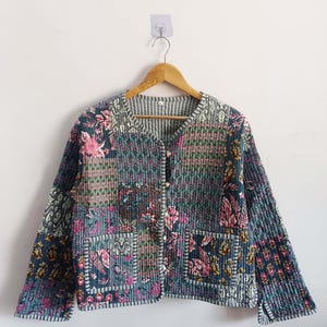 Op de afbeelding: Een blauw gewatteerd jack met een bloemenprint en een knoopsluiting. Het jack heeft twee zakken aan de voorkant.