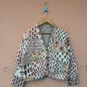 May include: A quilted jacket with a patchwork design. The jacket features a V-neck, long sleeves, and a button-up front. The patchwork includes floral and geometric patterns in various colors, set against a white background. The interior lining is striped.