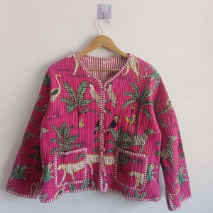 May include: A quilted jacket in a vibrant pink hue, adorned with a tropical print featuring zebras, leopards, birds, and lush foliage. The jacket has a V-neck, two pockets, and a button closure. The lining is striped.