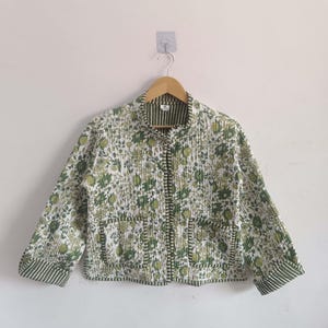 May include: A white and green floral print quilted jacket with a mandarin collar and long sleeves. The jacket has a button closure and two pockets.