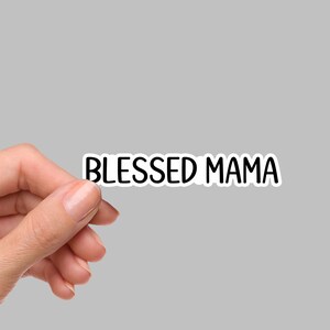 May include: A die-cut vinyl sticker featuring the text BLESSED MAMA in a bold, black, sans-serif font. The lettering is set against a clean white background, creating a high-contrast design that is clearly legible and simple in its presentation.