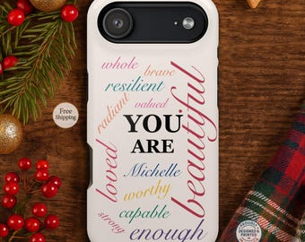 May include: A white phone case with a black camera lens area. The case features the words "YOU ARE" in a central position, surrounded by words like "beautiful", "worthy", and "enough" in various colors. The phrase "Proudly Designed & Printed in America" is also visible.