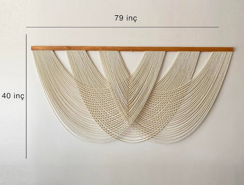May include: A white macrame wall hanging with a wooden dowel at the top. The hanging is 79 inches wide and 40 inches tall.