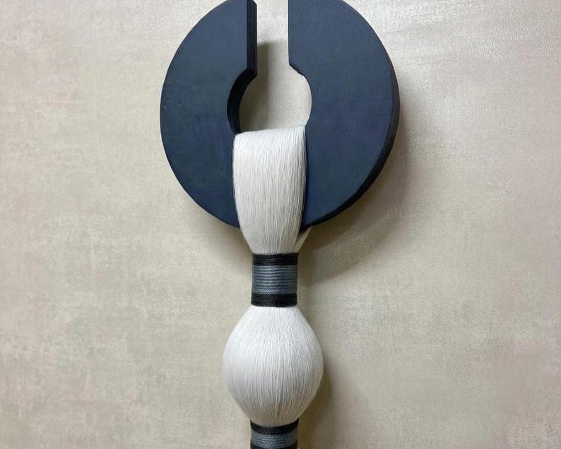 May include: A modern wall hanging featuring a dark blue, semi-circular wooden element with a central cutout. A white, textured, cylindrical element is suspended below, accented with dark gray and black bands. The piece has a minimalist, abstract design.