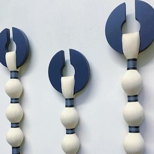 May include: Three abstract wall sculptures. Each features a navy blue semi-circle with a vertical slit, connected to a series of white, spherical forms. The forms are bound with dark blue bands, creating a modern, artistic display.