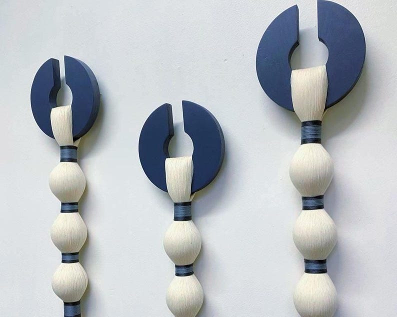 May include: Three abstract wall sculptures. Each features a navy blue semi-circle with a vertical slit, connected to a series of white, spherical forms. The forms are bound with dark blue bands, creating a modern, artistic display.