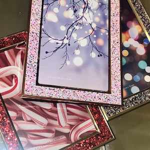 Può includere: Tre cornici per foto con glitter, una rosa, una rossa e una argentata. La cornice rosa contiene una foto di un ramo d'albero con luci bokeh, la cornice rossa ha bastoncini di zucchero e la cornice argentata ha luci bokeh. Ogni cornice misura 10 cm x 15 cm.