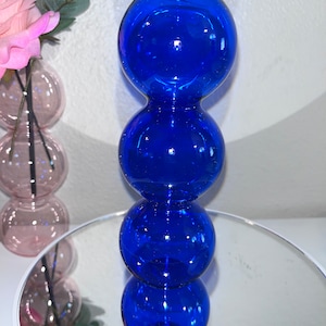 May include: A blue glass vase with a unique bubble design. The vase is made of four stacked spheres, each with a smooth, rounded surface.