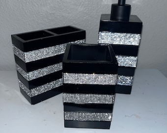 Puede incluir: Conjunto de accesorios de baño negros con un dispensador de jabón, un portacepillos de dientes y un vaso. Cada pieza presenta una base negra con una banda de brillantes brillantes.