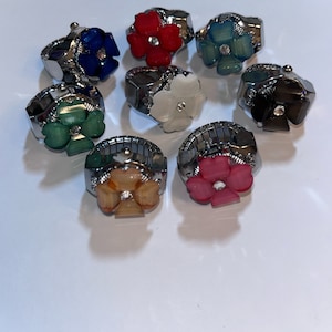 May include: Eight adjustable rings with flower-shaped charms in various colours, including red, blue, green, white, pink, and black.